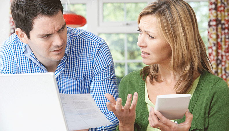 distressed couple seated at table reviewing bills